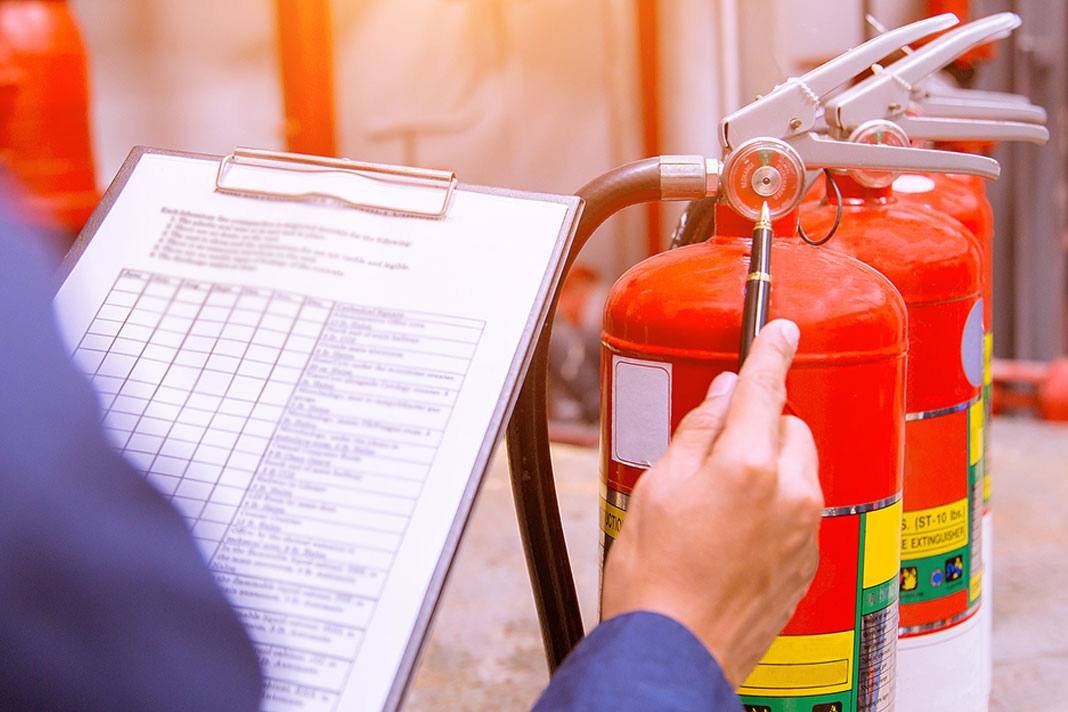 Técnico com prancheta conferindo manômetro e lacre de extintores